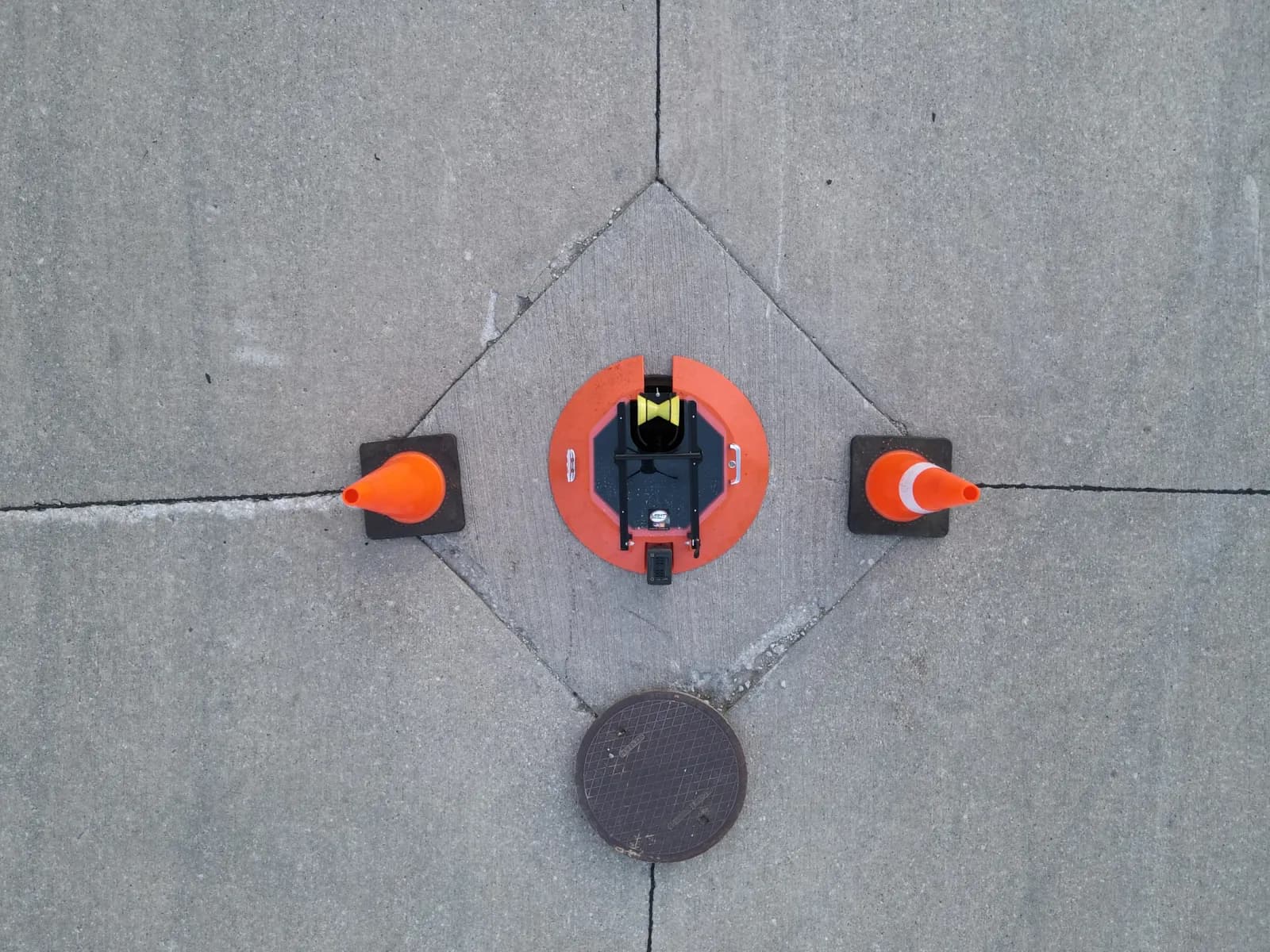 Orange Light Ring over a street manhole between two cones, with the removed lid nearby.